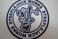白地に紺色の縁取りがある円形のオリジナルプリントワッペンの制作事例。周囲に“STEEPLEJACK WORKS”の文字が円形に配置されている。