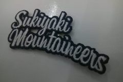 文字だけの構成で印象的なグループロゴのオリジナル刺繡ワッペンの制作事例。複雑な外周を見事にカットした高度なヒートカット技術もうかがえる。