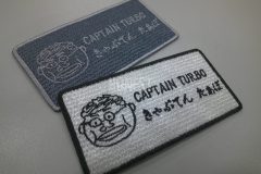 手書き風のイラストを刺繍したオリジナル刺繡ワッペンの制作事例。灰色生地と白生地との２色展開。