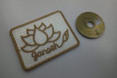 ５円硬貨のタテ寸1.2倍ほどのミニマムな白生地に金糸で蓮の花をモチーフにした花が刺繍されたオリジナルワッペンの制作事例。