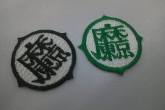 円の外周が少しギザギザした飾り縁が印象的な丸い形のオリジナル刺繍ワッペンの制作実績。白地×黒糸、白地×緑の２色展開。