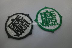 円の外周が少しギザギザした飾り縁が印象的な丸い形のオリジナル刺繍ワッペンの制作実績。白地×黒糸、白地×緑の２色展開。