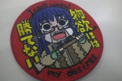 赤い円形のワッペン。中央に青髪で眼鏡をかけたアニメ風キャラクターが叫ぶような表情で描かれたオリジナル刺繡ワッペンの制作見本。