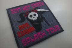 灰色地に黒い縁取りの刺繍ワッペン。中央に白いドクロ顔のキャラクターが黒いローブをまとい、赤いリボンをつけて鎌を持つ姿が描かれたオリジナル刺繡ワッペンの制作事例。