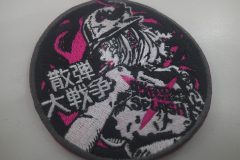 サバゲーの装備を付けた煙草をくわえた女性の振り向きざまの姿をモノクロで刺繡したオリジナル刺繡ワッペンの制作実績。ショッキングピンクでアクセントを付けてイラストと「散弾大戦争」の文字を際立たせた作品。