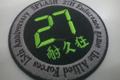 黒い生地にネオン系の黄緑色の糸で大きく27の数字と文字を中央に配置し、周りをグレーで太くタタミ縫いをしその上から大会名などを刺繡した、オリジナル刺繡ワッペンの制作実績。