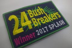 黒色の生地の上段に黄緑色の破裂した円のようなイラストの上に大きく24と「Bush Breakers」の文字を重ねるように黄色で刺繍し、下段に開催時期や会場を刺繡したオリジナル刺繡ワッペンの制作実績。
