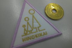 白のアーバンツイルに保育園のスッキリとしたロゴをマットゴールドと薄いピンクでシンプルに加工した刺繍ワッペンの制作事例。