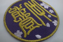 紫のエンブクロス生地に煌びやかな金糸をメインに剣道道場のロゴを刺繍した、オリジナルワッペンの制作事例。