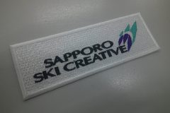 白のエンブクロス生地をベースにスキー用品店のオリジナルロゴを刺繡ワッペンとして製作した加工事例。