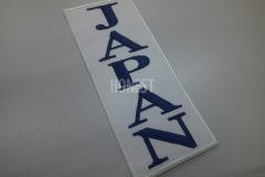 白色のツイル生地に紺色の糸で縦書きでJAPANの文字のみを刺繡した、シンプルなデザインのオリジナル刺繡ワッペンの制作事例。