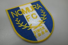 白色の生地に青色で背景を付け、月桂冠どサッカーチーム名を刺繡した、オリジナルワッペンの制作事例。