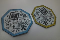 八角形の白い生地に黒糸で細かいデザインの刺繍を施したオリジナルワッペン。縁取りが水色と黄色の二色展開の作品。