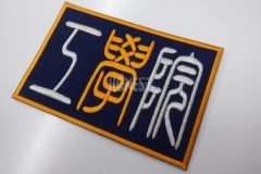 濃紺のベース生地に学校名を白糸とオレンジの糸でシンプルに刺繍をした、刺繍ワッペンの制作事例。