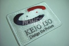 白のエンブクロス紀伊\時に濃紺と赤・グレーの三色で大学のロゴを刺繍した、オリジナル刺繍ワッペンの制作事例。