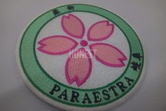 白地の円形にピンクの花と緑の縁、周囲に日本語表記と『PARAESTRA』の文字が刺繍された柔術クラブのオリジナル刺繡ワッペンの制作見本。
