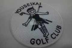 眼鏡のおじさんがゴルフクラブを羽に見立てた妖精の恰好をしているイラストの刺繡ワッペン。チーム名に由来した妖精が特徴の作品。