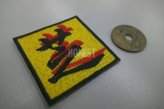 黄色のクロス生地に黒と赤でズレて重なるデザインの芝の文字が刺繡された、オリジナル刺繡ワッペンの制作事例。