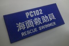 青色のツイル生地に白糸で大きく文字を刺繡した長方形のオリジナル刺繡ワッペンの制作実績。