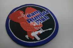 赤い魚が不敵な笑みを浮かべながらライフル銃を構えているイラストとチーム名を刺繡した、オリジナル刺繡ワッペンの制作実績。