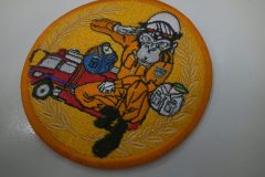 オレンジ色の生地に消防車と消防服を着たサルのイラストを大きく刺繡した、オリジナル刺繡ワッペンの制作実績。