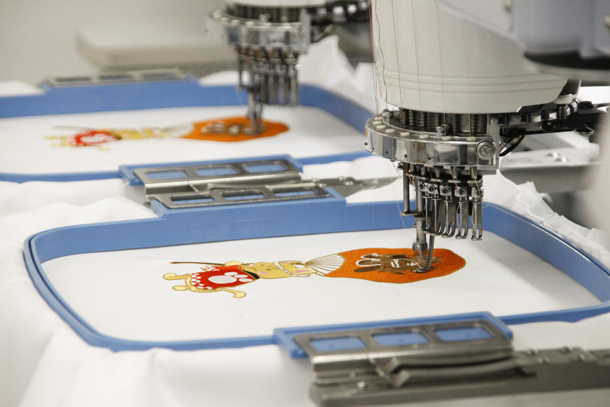 「祭」の文字が大きく描かれた、大きな団扇を持ったキャラクターをビッグサイズ刺繍している作業風景。