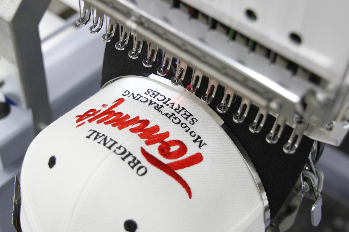 白のベースボールキャップの前面にアメリカンクラシックな赤と黒の刺繍を加工する作業工程。