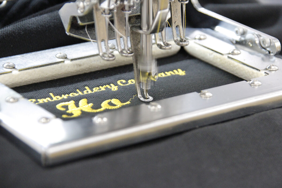 黒のパーカーに金糸で店名を刺繍している作業工程。