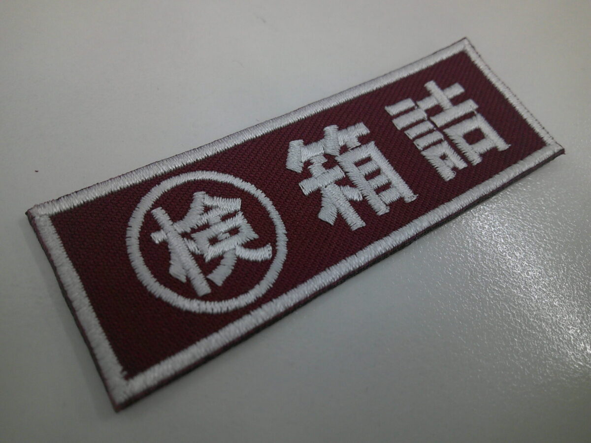 エンジの生地に太ゴシック体・白糸で箱詰の文字を縫った、もったいないワッペンの制作事例。