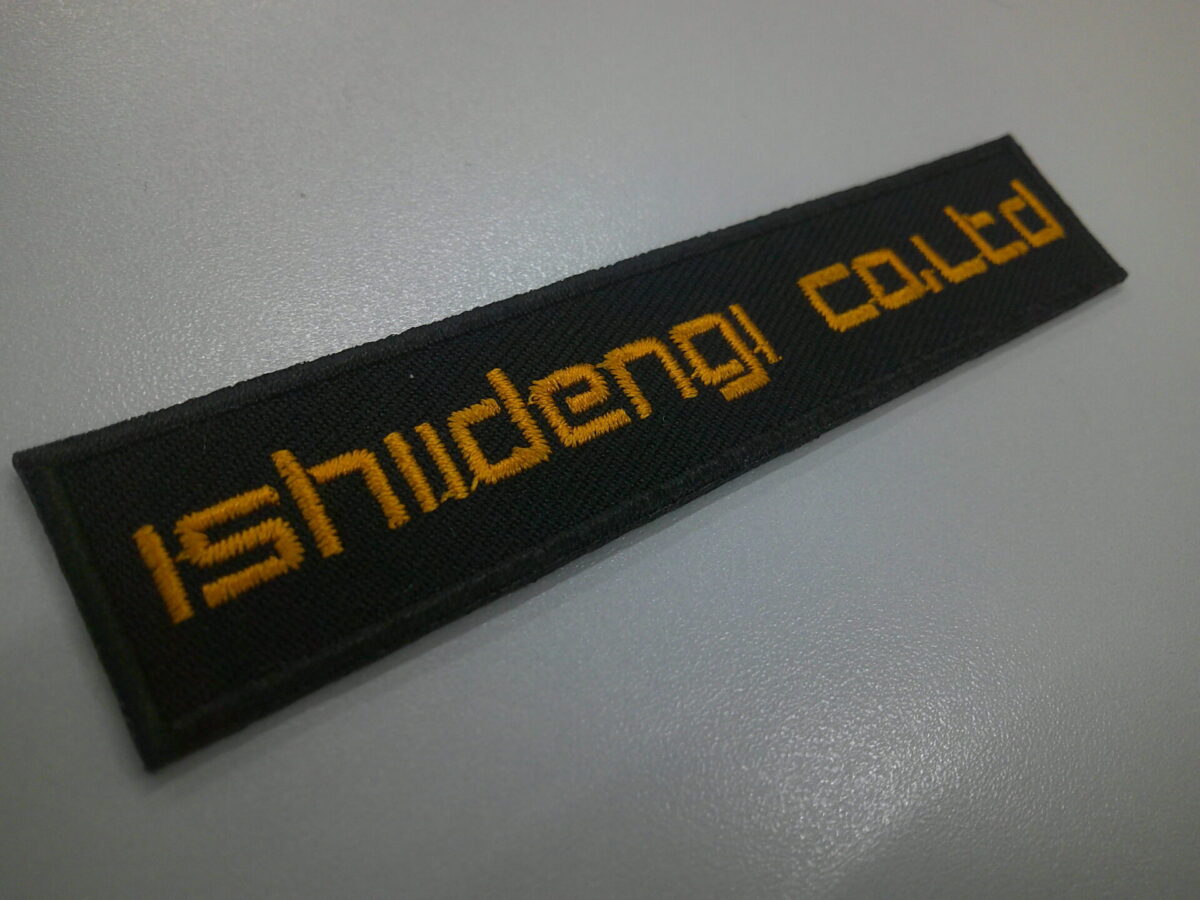 企業様の文字ワッペン。黒ベースにオレンジ文字。オリジナルフォントで製作。