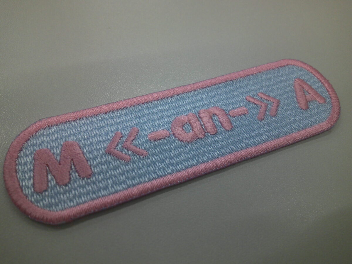 日本医科大学の文字ワッペン。薄サックスブルーに柔らかなピンクの糸でアルファベットと記号で製作した実績。