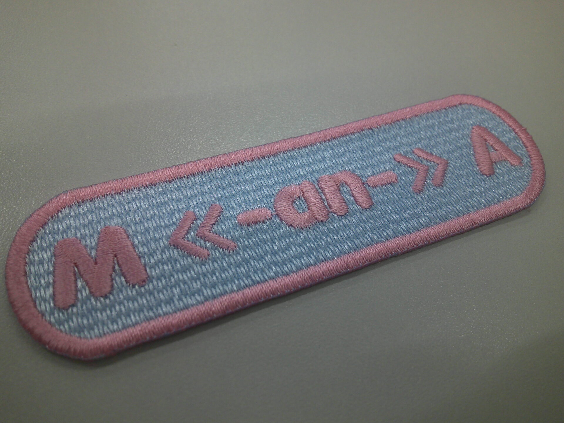 日本医科大学の文字ワッペン。薄サックスブルーに柔らかなピンクの糸でアルファベットと記号で製作した実績。