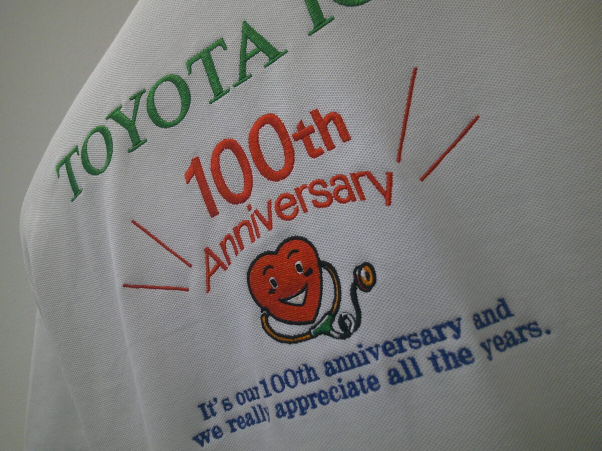 総合病院様の100周年記念ロゴを白ポロシャツの背面に大きく刺繍した制作実績。