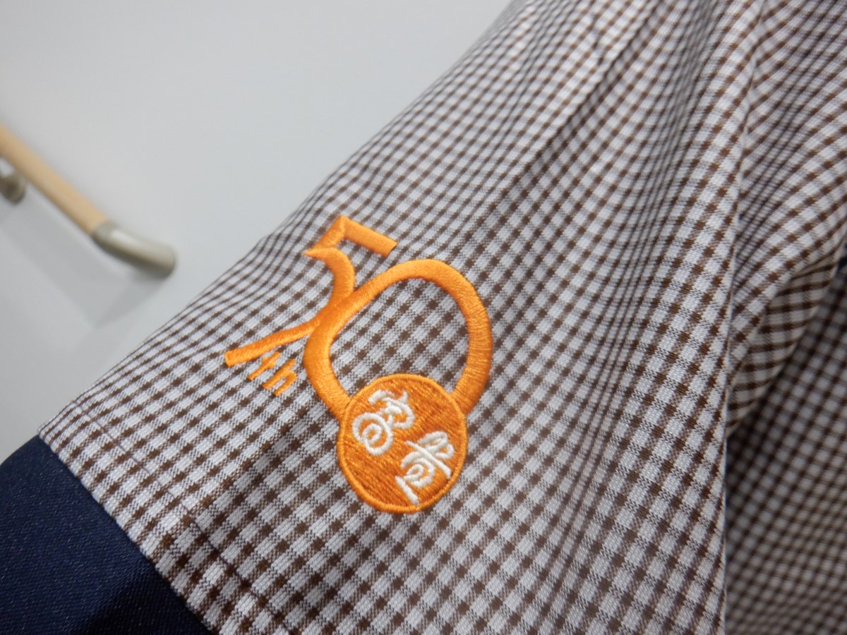 チュニック左袖口に企業様の50周年記念ロゴをオレンジ糸で刺繍した制作実績。