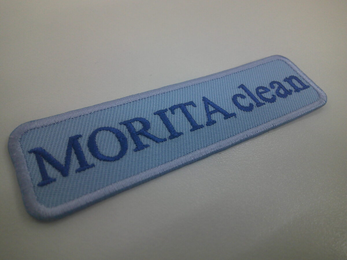 水色の生地をベースにロイヤルブルーの糸で文字を刺繍した、文字ワッペンの制作実績。
