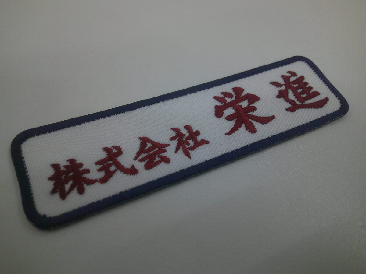 白のツイル生地にワインレッドの色で会社名を刺繍した、文字ワッペンの制作実績。