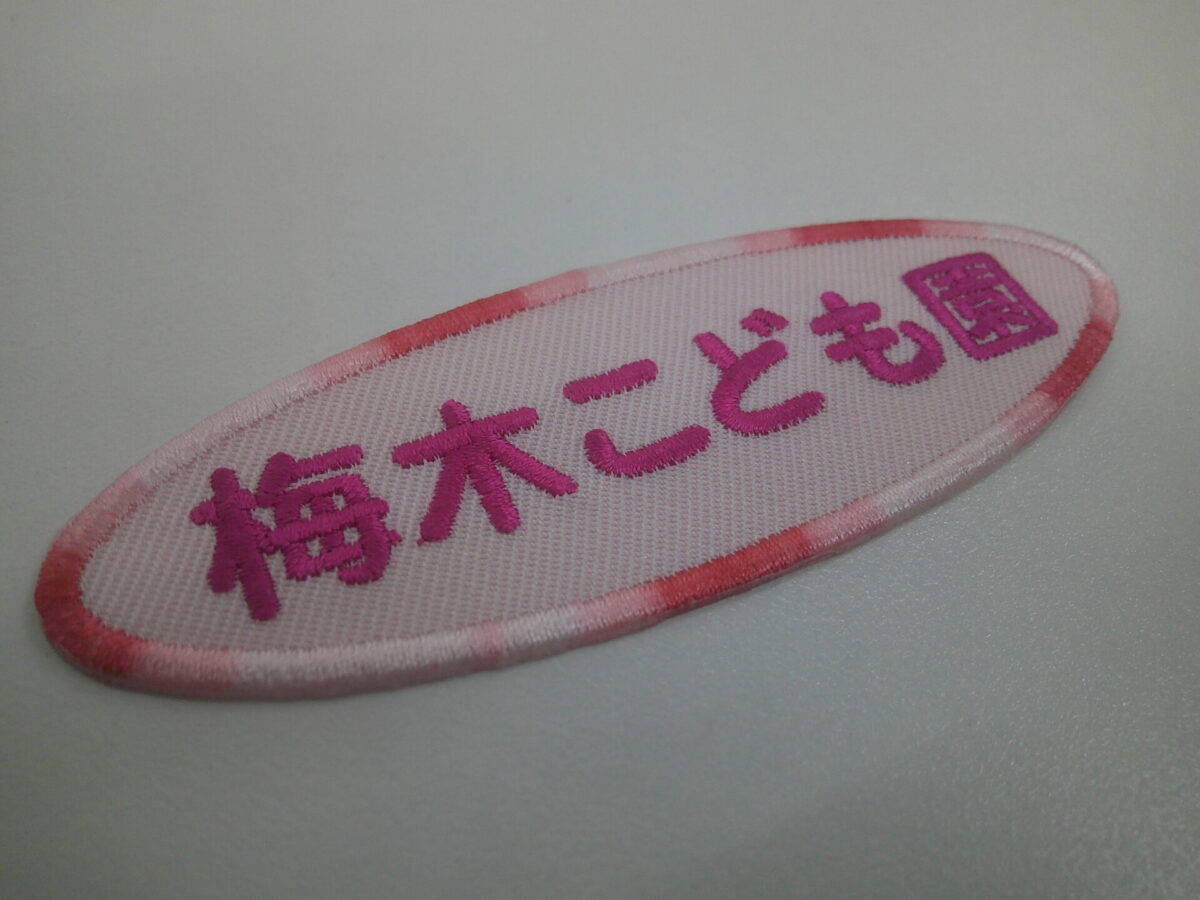 薄いピンクの生地に濃いめのピンクで園名を刺繍。外周フチにはグラデーション糸を使用した文字ワッペンの制作実績。