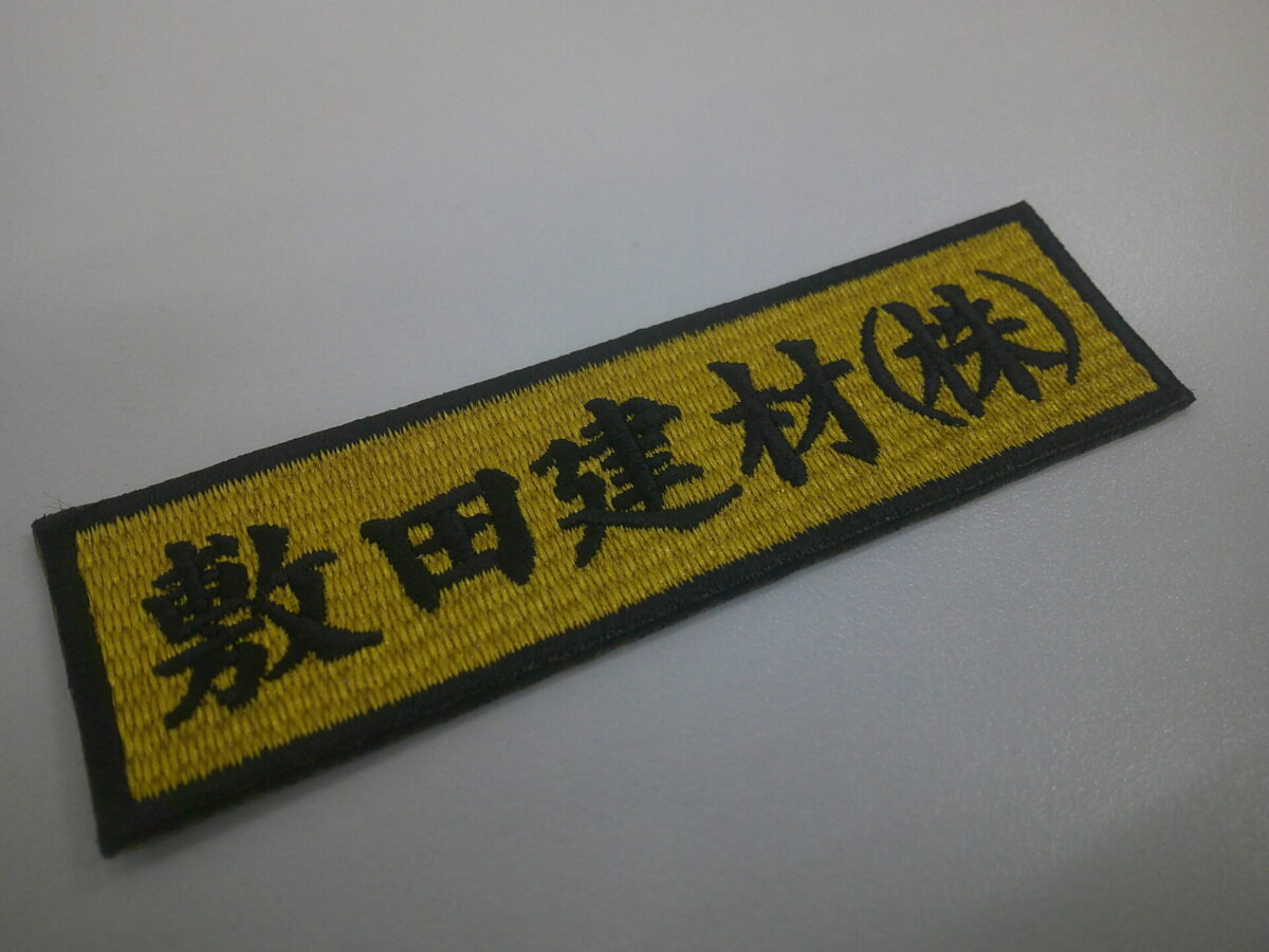 マットゴールドの生地に黒糸で会社名を刺繍した、文字ワッペンの制作実績。