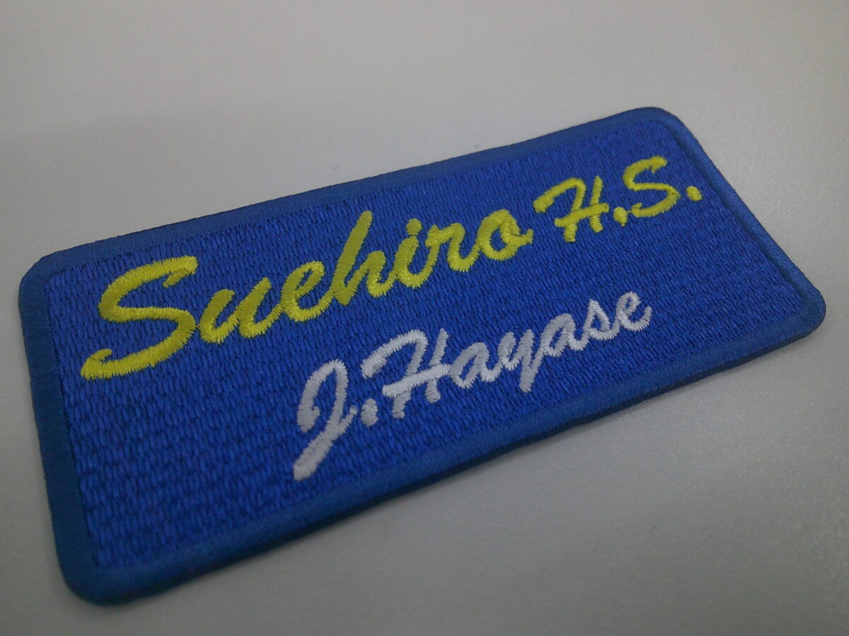 青のエンブクロス生地にレモンイエローとホワイトで文字を刺繍した、文字ワッペンの制作実績。