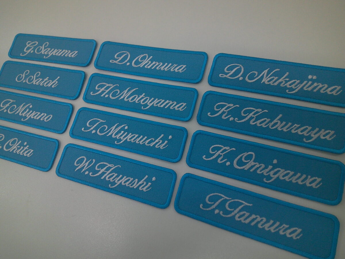 チームでそれぞれの個人名入りの文字ワッペンを制作した実績。ターコイズ生地に白文字。