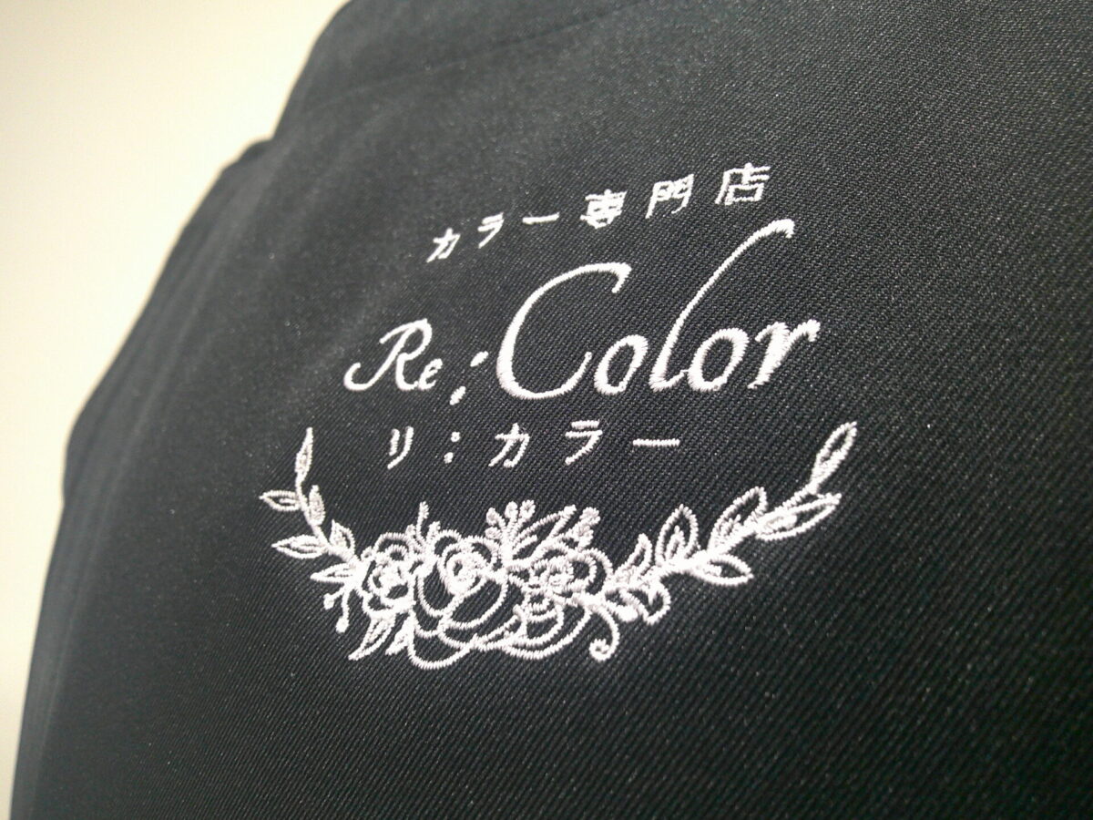 エプロン(FK7168)の左胸に白糸で美容室のロゴ刺繍(フローラルデザイン)を加工した制作事例|アップ