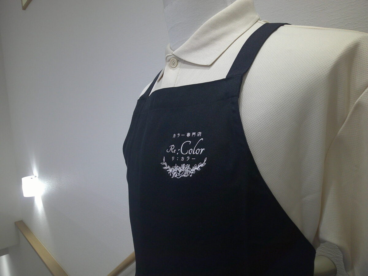 エプロン(FK7168)の左胸に白糸で美容室のロゴ刺繍(フローラルデザイン)を加工した制作事例|斜めアングル