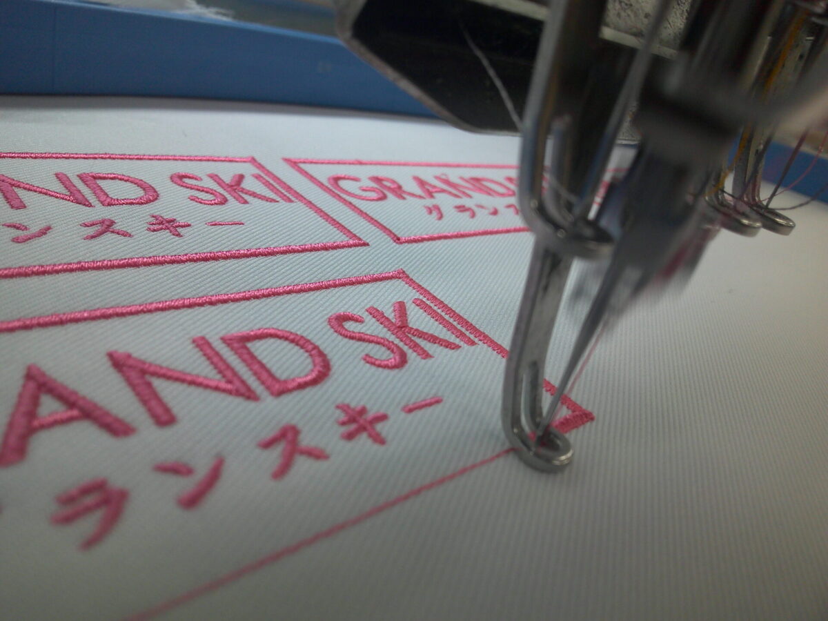 白のアーバンツイルにピンクの糸で文字と外周フチを刺繍している作業工程。