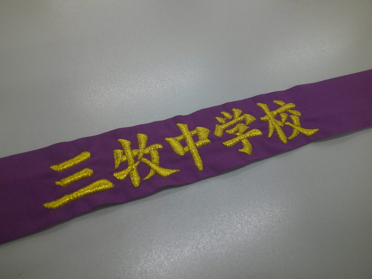 紫のハチマキに金糸で学校名を刺繍した制作事例。
