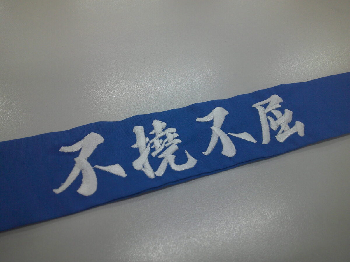 青のハチマキに白糸で不撓不屈と、行書体で刺繍をした制作事例。