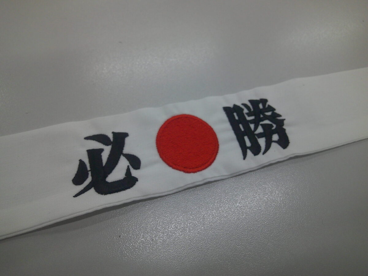 白のハチマキに黒糸で「必勝」と刺繍。その文字の間に日の丸を赤糸で刺繍した制作事例。